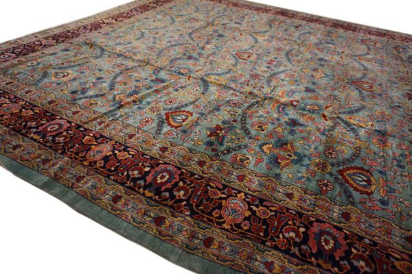 Low-pile rug with a teal field, featuring intricate red, blue, and gold floral patterns and a wide dark border.