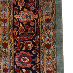Detail of a traditional rug showing navy field, dense floral design, multicolor border, and solid green edge.