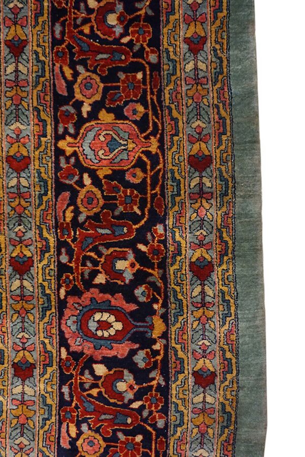 Detail of a traditional rug showing navy field, dense floral design, multicolor border, and solid green edge.