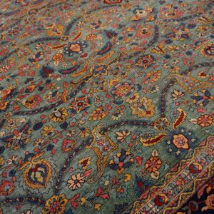 A traditional low-pile rug with a teal field and dense floral motifs in red, navy, and gold.