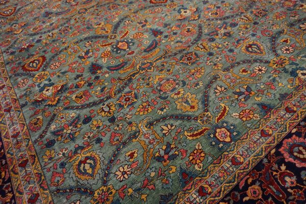 A traditional low-pile rug with a teal field and dense floral motifs in red, navy, and gold.