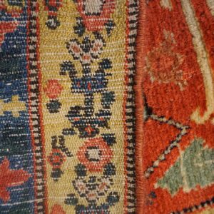 Extreme close-up of textured rugs joined, displaying geometric patterns in blue, gold, red, and shaggy green.