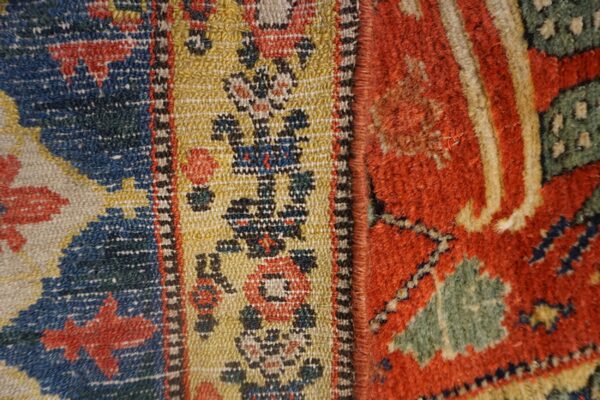 Extreme close-up of textured rugs joined, displaying geometric patterns in blue, gold, red, and shaggy green.