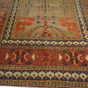 Low pile rug featuring a tan field with rust patterns, surrounded by complex red and dark blue borders.