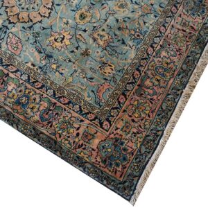 Close-up of an intricate floral rug pattern in seafoam blue, salmon, and navy, with visible fringe.