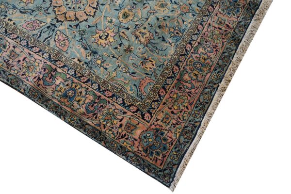 Close-up of an intricate floral rug pattern in seafoam blue, salmon, and navy, with visible fringe.