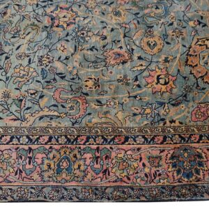 Low-pile rug showing an all-over floral design in teal, pink, rust, and navy, including a wide pink border.