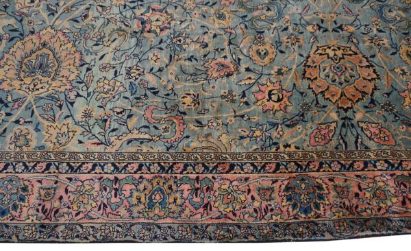 Low-pile rug showing an all-over floral design in teal, pink, rust, and navy, including a wide pink border.