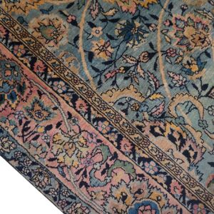 Ornate area rug detail with a sage blue field and a rose border featuring detailed floral and vine patterns.