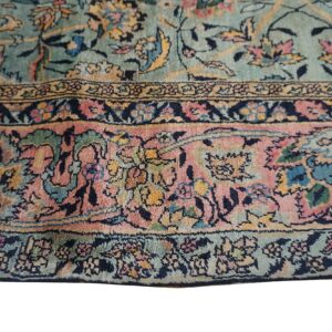 Ornate floral rug detail showing a teal field and wide borders in pink, yellow, and navy.