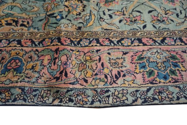 Ornate floral rug detail showing a teal field and wide borders in pink, yellow, and navy.