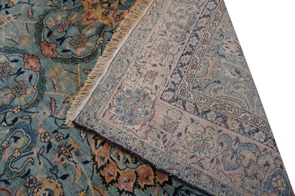 The teal, pink, and gold patterned rug face is displayed next to its muted, flatwoven reverse side and fringe.