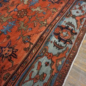Terracotta and blue patterned rug with low pile lying on weathered gray wood flooring.