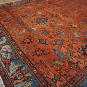 Distressed rust-colored rug with complex blue and green motifs and a contrasting light blue border on wood.