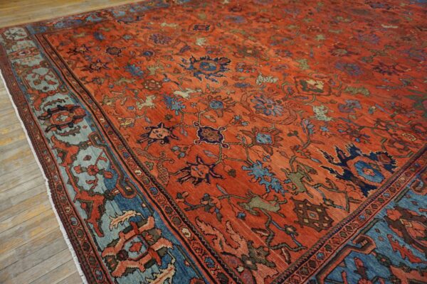 Distressed rust-colored rug with complex blue and green motifs and a contrasting light blue border on wood.