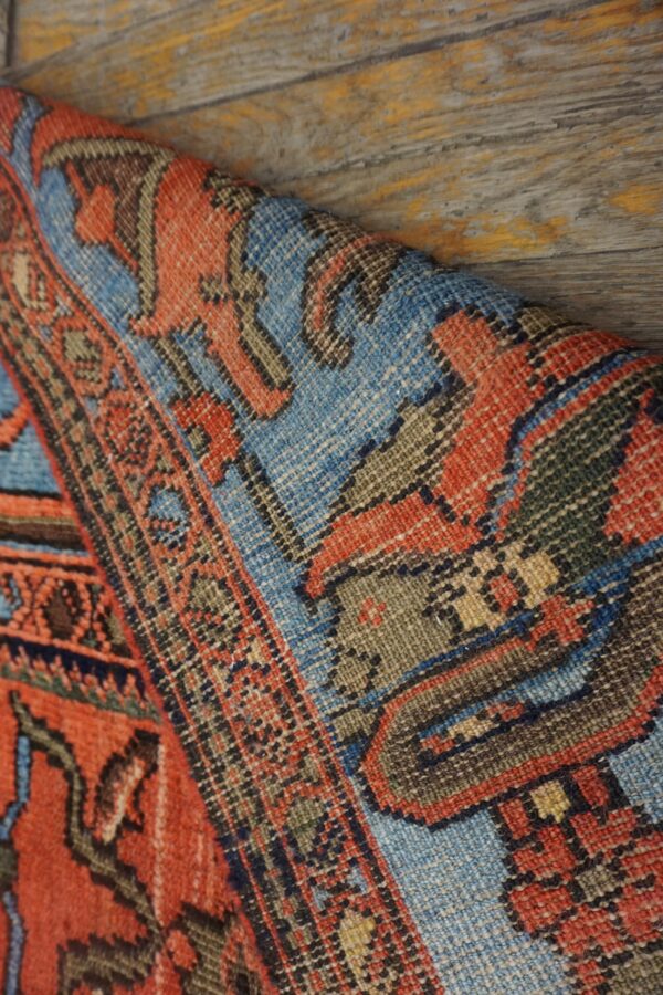 A rolled, low-pile rug with geometric blue and orange designs rests against distressed wooden flooring.