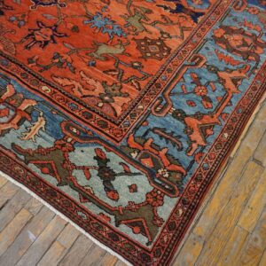 Ornate red field rug with blue and green motifs rests on worn, yellowed wood plank flooring.