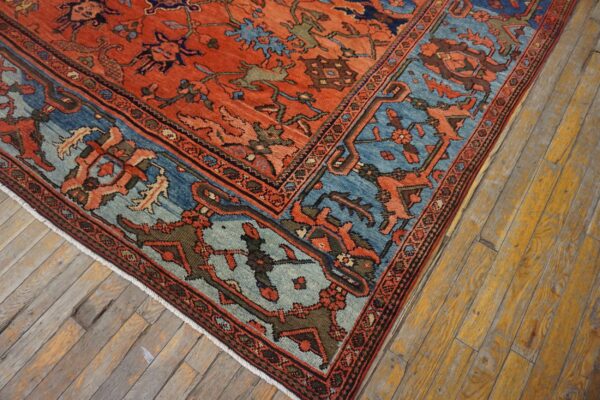 Ornate red field rug with blue and green motifs rests on worn, yellowed wood plank flooring.