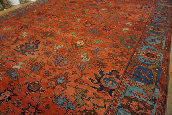 Intricate rust-colored area rug features an all-over floral and animal pattern with a wide blue geometric border.