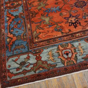 Rustic orange and blue patterned rug corner lying on distressed light wood plank flooring.