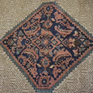 Detail of a rug with a complex navy and rust diamond medallion bordered by a textured beige geometric field.