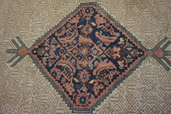 Detail of a rug with a complex navy and rust diamond medallion bordered by a textured beige geometric field.
