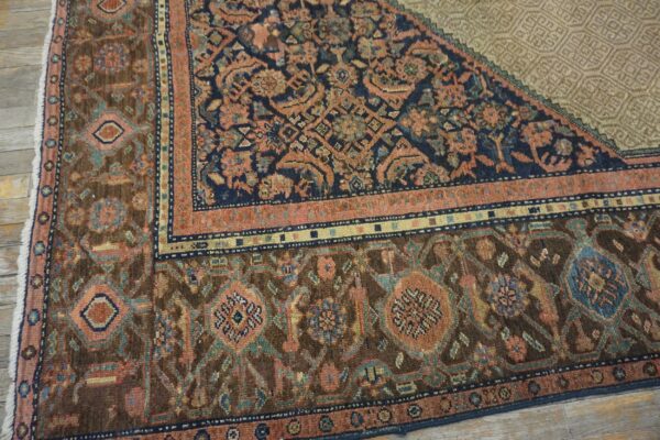 Close-up of a traditional rug corner showing dark brown, navy, coral, and blue patterns on light wood flooring.
