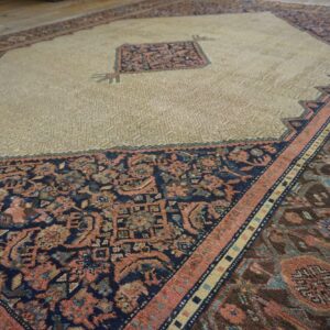 Beige central field with geometric texture surrounded by dark, complex floral borders on wooden flooring.