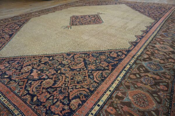 Beige central field with geometric texture surrounded by dark, complex floral borders on wooden flooring.