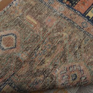Close-up of a tightly woven rug backing with multicolored threads folded over distressed wood flooring.