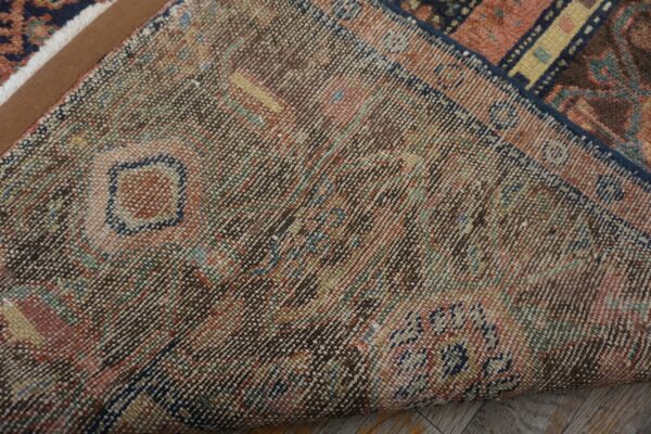 Close-up of a tightly woven rug backing with multicolored threads folded over distressed wood flooring.