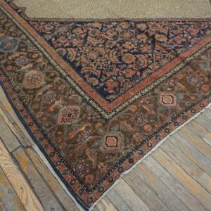 Corner of a traditional brown, navy, and pink rug displayed on distressed light wood flooring.