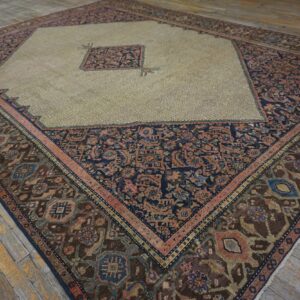 Multi-colored diamond rug with a light khaki field and dark borders rests on worn plank flooring.