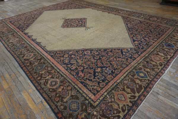 Multi-colored diamond rug with a light khaki field and dark borders rests on worn plank flooring.