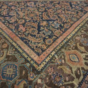 Close-up of a traditional rug border in navy, salmon pink, brown, and teal on distressed wood floors.