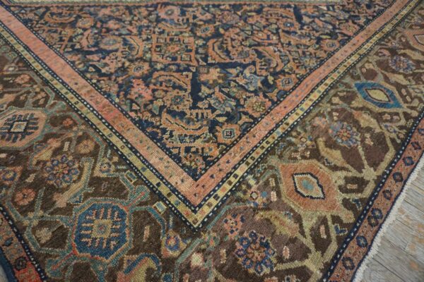Close-up of a traditional rug border in navy, salmon pink, brown, and teal on distressed wood floors.
