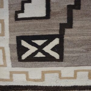 Close-up of a flatweave rug with geometric patterns in cream, tan, gray, and dark brown.