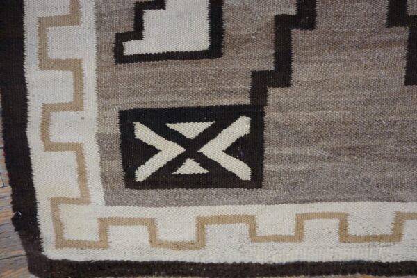 Close-up of a flatweave rug with geometric patterns in cream, tan, gray, and dark brown.