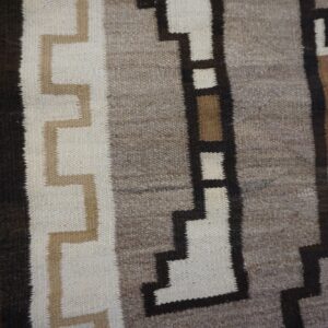 Geometric flat-weave rug featuring bands of gray, white, and stepped brown patterns on weathered wood flooring.