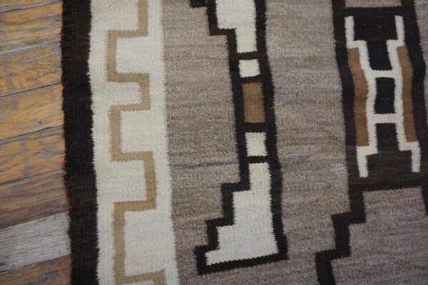 Geometric flat-weave rug featuring bands of gray, white, and stepped brown patterns on weathered wood flooring.