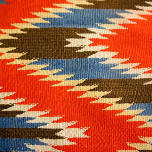 Close view of a flatweave rug featuring sharp zigzags in red, blue, brown, and off-white.