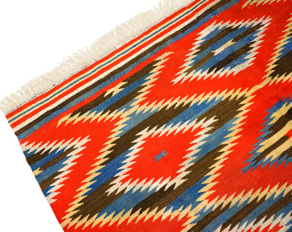 Flatwoven rug with a bold geometric pattern of red, blue, brown, and white zigzags, featuring white fringe.