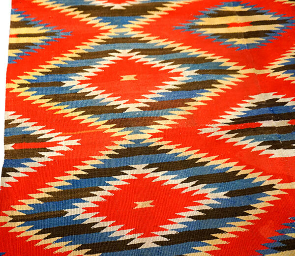 Flat-weave rug with geometric patterns of red, blue, black, and cream serrated diamonds.