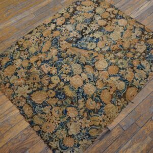 Muted floral rug featuring gold and blue tones placed diagonally on distressed wood flooring.
