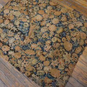 Worn, low-pile rug fragment featuring dense blue, beige, and peach florals rests on weathered wood planks.