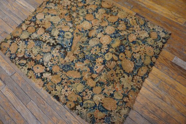 Worn, low-pile rug fragment featuring dense blue, beige, and peach florals rests on weathered wood planks.