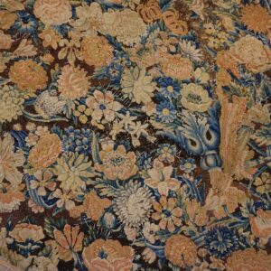 Worn floral rug fragment in tan, blue, and peach with visible stitching rests on brown wood planks.