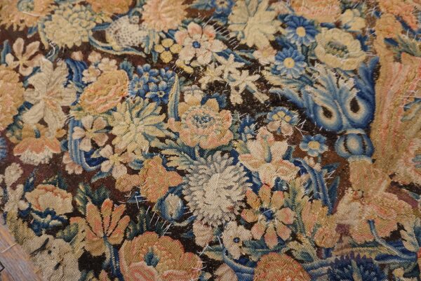 Worn tapestry featuring a dense floral pattern in blue, gold, and pink with visible white stitching repairs.