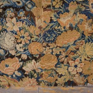 Frayed low-pile floral rug displaying dense gold, peach, and blue patterns over dark brown ground on wood.