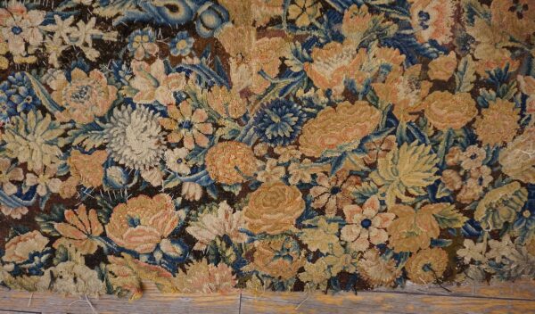Worn tapestry featuring a dense floral pattern in muted gold, cream, blue, and dark brown.
